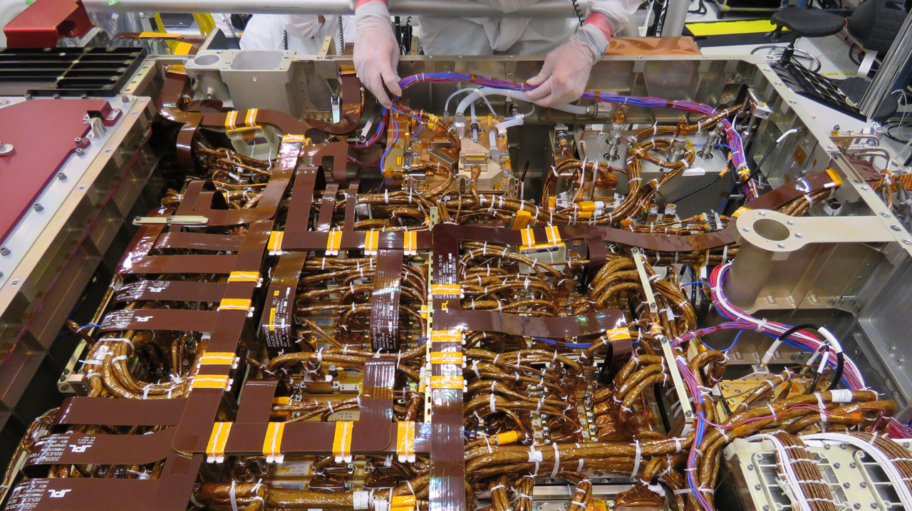 An engineer works on the exposed belly of the Mars 2020 rover